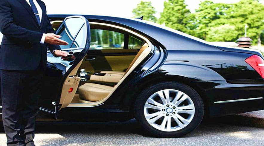 Businessman in suit standing by open door of black luxury sedan with beige interior and silver alloy wheels